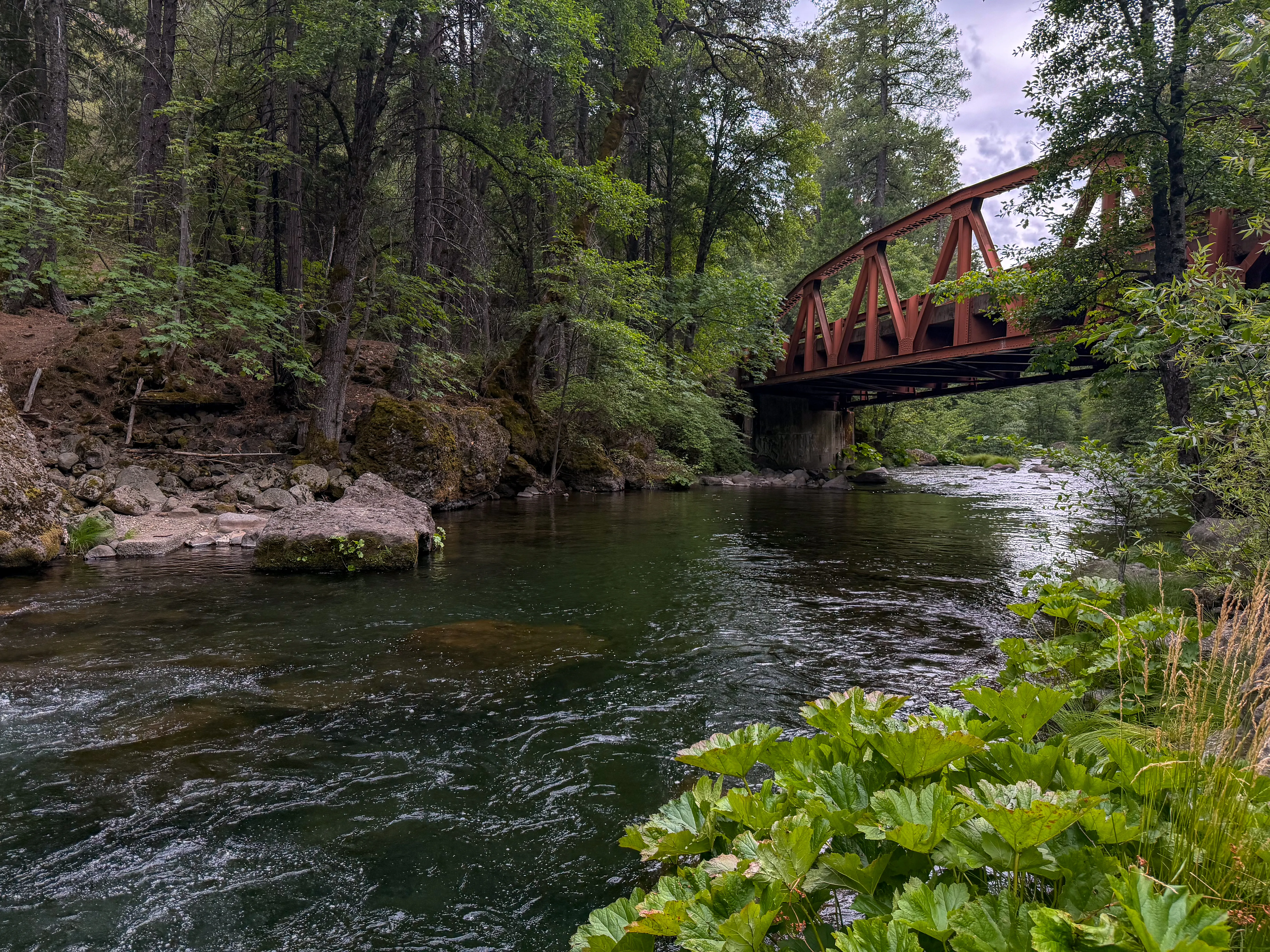 The rust-colored truss bridge over Deer Creek, framed by dense green forest